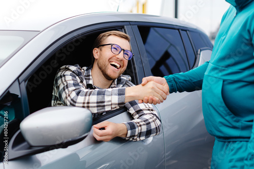 Man buying car and shaking hands with salesman against blurred auto, closeup. Concept of choosing and buying new car at showroom