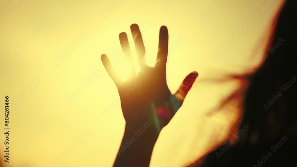 hand of happy girl at sunset with glittering golden light. sunset between the hands of a girl. this happy girl stretches her hand to the sun. girl silhouette stretches out her hand to dream the sun