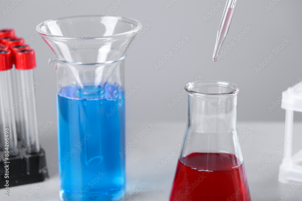 Dripping liquid from pipette into flask on grey background, closeup Dripping liquid from pipette into flask on grey background, closeup