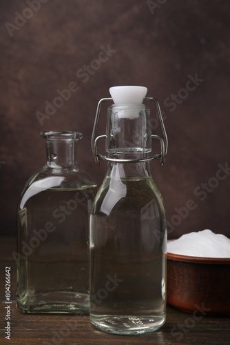 Vinegar in glass bottles and baking soda on wooden table