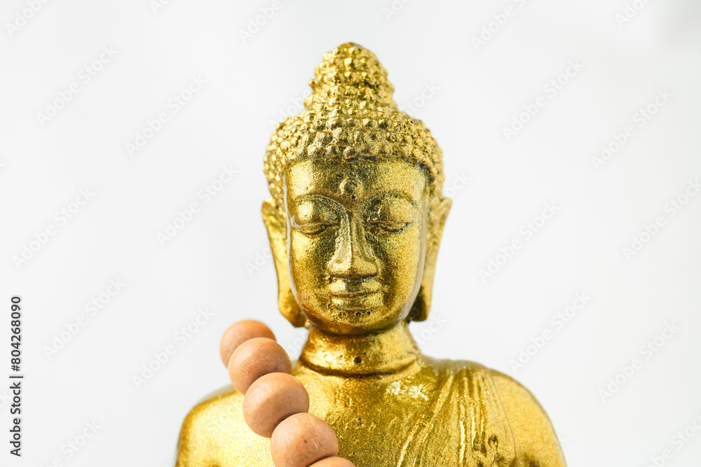 A golden statue of a Buddhist figure meditating and wearing prayer beads facing the front isolated on white background. Concept for Vesak Day and Enlightenment Day