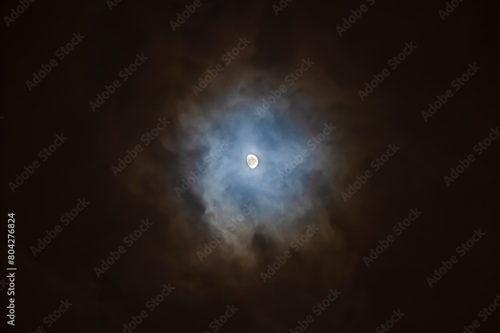 The Moon is surrounded by colorful glowing clouds in the dark night sky. Night sky scene The Moon is surrounded by colorful glowing clouds in the dark night sky. Night sky scene