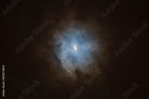The Moon is surrounded by colorful glowing clouds in the dark night sky. Night sky scene
