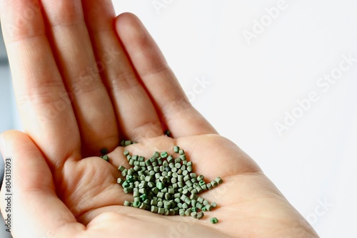 Kunststoffgranulat (grün) in einer Hand vor weißem Hintergrund Closeup, Kunststoff als Rohstoff für die Plastik Herstellung und Kunststoffverarbeitung und als Recyclingmaterial