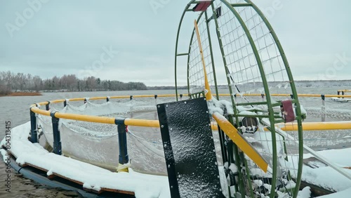 Fish farm exterior. Airboat with propeller on the background of snow-covered reservoir and fish cages in winter.