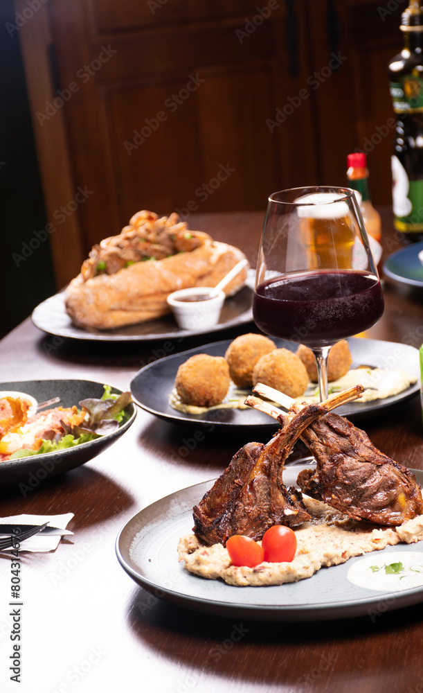 dinner at a steakhouse with rack of lamb with mashed potatoes and cherry tomatoes and glass of red wine and craft beers and blurred background