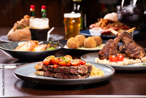 dinner banquet table in a steakhouse with sirloin steak and farofa in focus and rack of lamb out of focus and other dishes