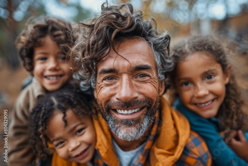 Man with curly gray hair and big smile taking a selfie with three happy children outdoors © Larisa AI