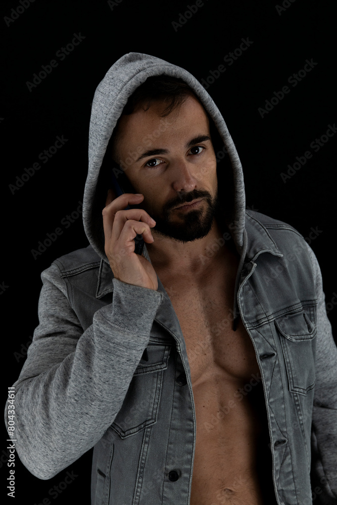 Strong shirtless man wearing jacket with the hood up and talking on the phone Strong shirtless man wearing jacket with the hood up and talking on the phone