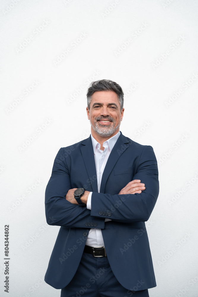 Smiling confident latin hispanic mature business man standing crossed arms isolated on white background. Hispanic older senior businessman professional ceo, coach, leader looking at camera. Vertical