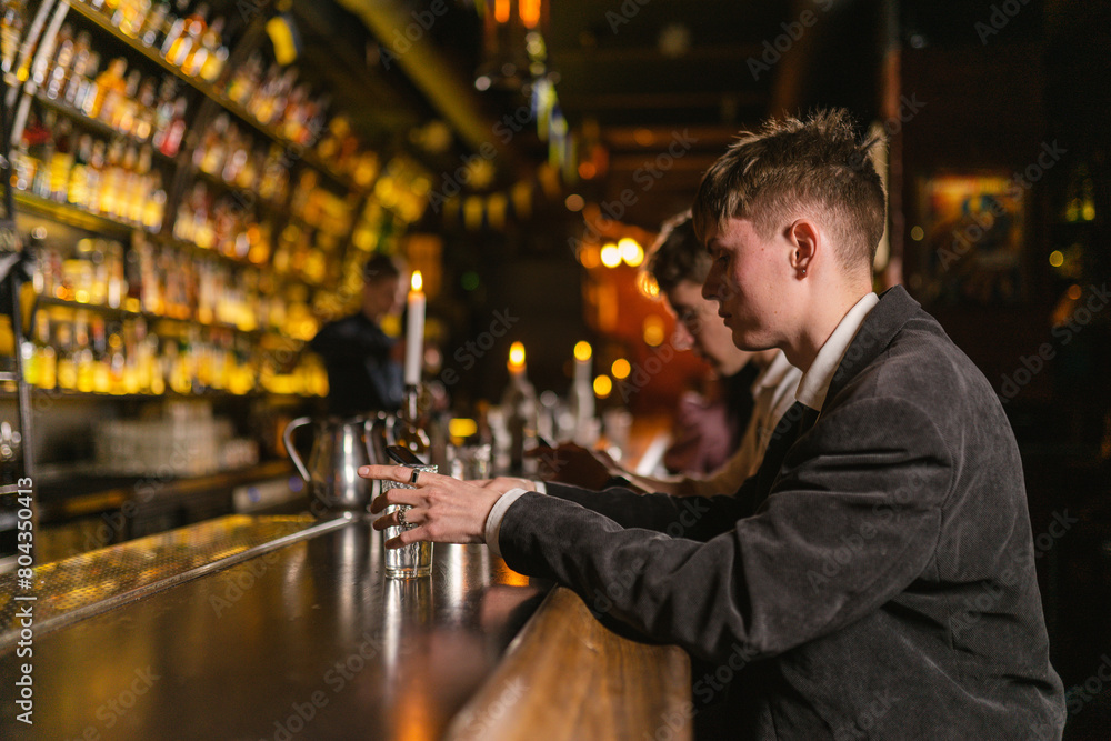 Man sits near wooden bar counter after noisy party in modern club. Handsome guy drinks various alcohol alone in cozy place
