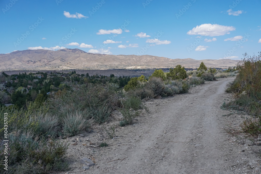 a dirt road going down the side of a hill with some mountains in the distance