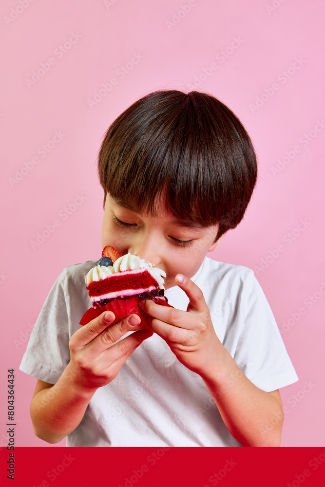 Delightful dessert time. Boy, kid enjoying delicious red velvet cake with cream and berries, making big bite against pink background. Concept of food, childhood, emotions, meal, menu, pop art Delightful dessert time. Boy, kid enjoying delicious red velvet cake with cream and berries, making big bite against pink background. Concept of food, childhood, emotions, meal, menu, pop art