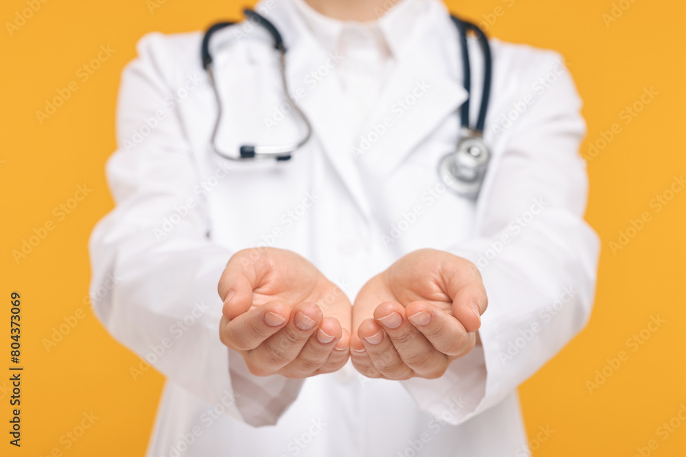 Doctor with stethoscope holding something on orange background, closeup Doctor with stethoscope holding something on orange background, closeup