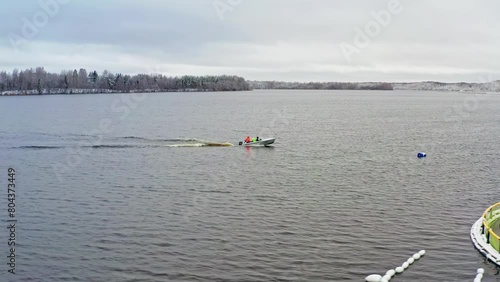 Winter Fish Farm Patrol. Anglers sail an iron motorboat on an open water fish farm in winter through snow-covered scenery. Aerial drone shot