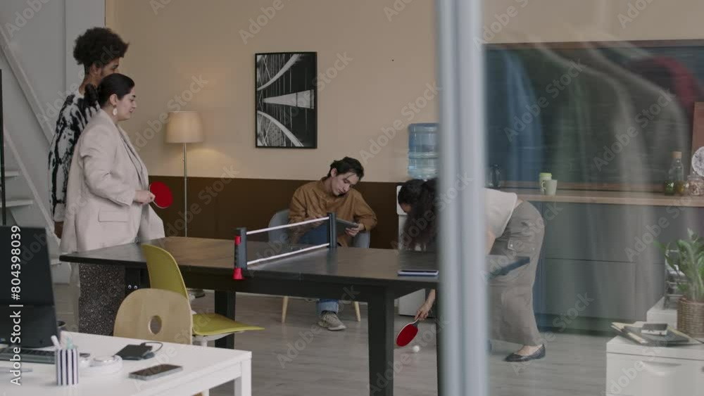 Young creative team of employees having fun playing table tennis and other activities while resting from work during lunchtime in contemporary office Young creative team of employees having fun playing table tennis and other activities while resting from work during lunchtime in contemporary office