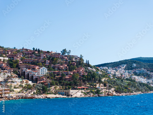 Fototapeta Naklejka Na Ścianę i Meble -  A picturesque coastal view of the hillside buildings in Kalkan, Turkey, overlooking the clear blue waters of the Mediterranean Sea.