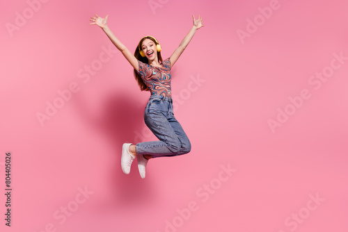 Full length photo of lovely teen lady jump raise hands headphones dressed stylish print clothes isolated on pink color background photo
