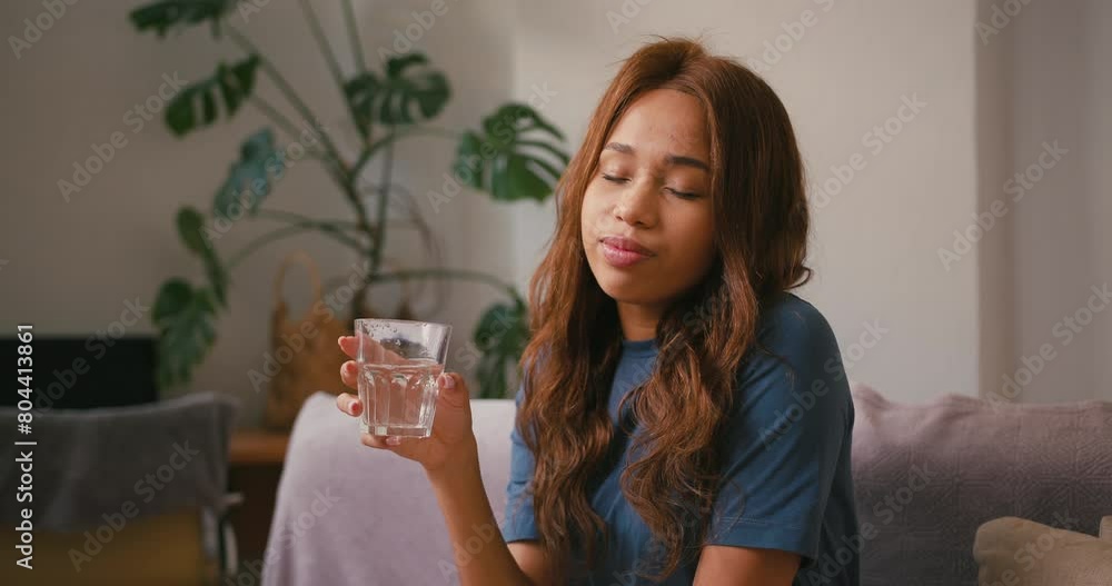 Young Hispanic woman drinks clean water sitting on sofa Young Hispanic woman drinks clean water sitting on sofa
