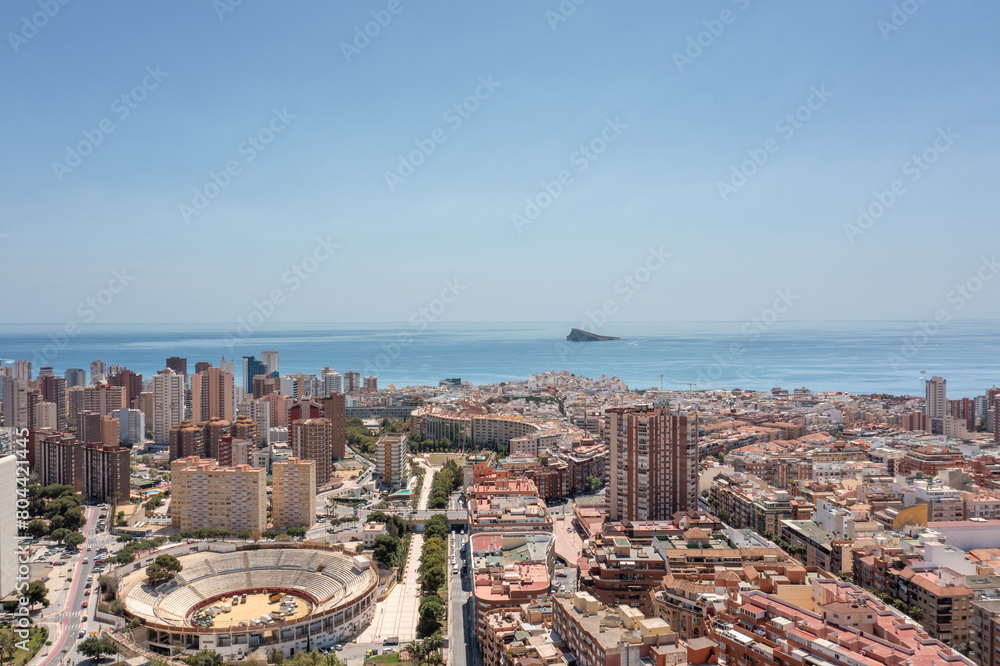 Aerial photo of the town of Benidorm in Spain showing buildings and apartments in the town and the old historical bull ring known as The Plaza De Toros Benidorm with the ocean in the background