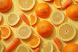 Fresh fruits and vegetables arrangement with oranges, carrots, and lemons on a vibrant yellow background viewed from above