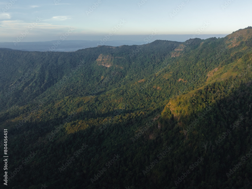 Obraz premium The fading light of dusk gently touches the slopes of a mountain blanketed with dense greenery, hinting at the vast wilderness.
