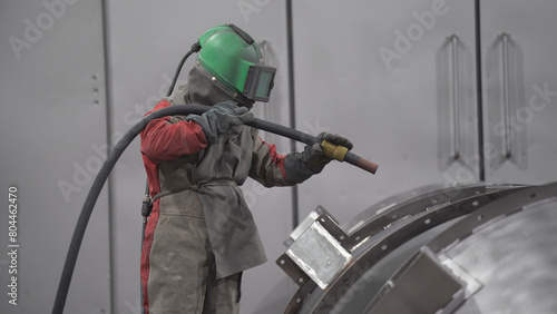 Masked worker is sandblasting or painting the product.
