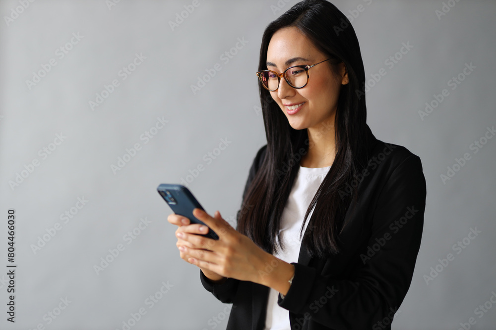 An Asian businesswoman typing a message on her smartphone, immersed in communication and technology. An Asian businesswoman typing a message on her smartphone, immersed in communication and technology.