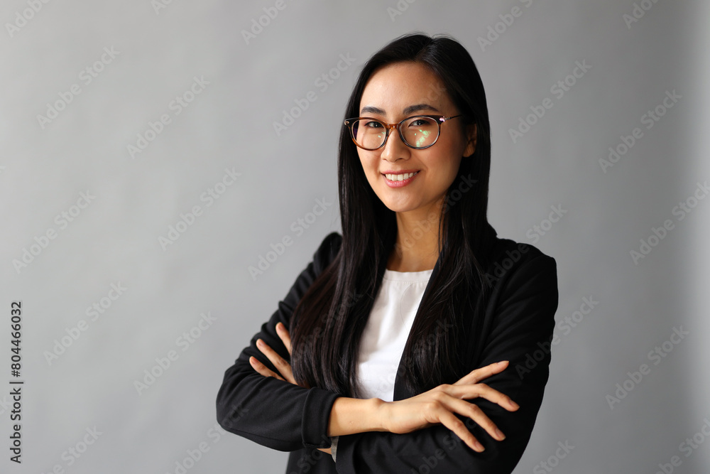 A successful Asian businesswoman in suit, radiating confidence and happiness against a grey background. A successful Asian businesswoman in suit, radiating confidence and happiness against a grey background.