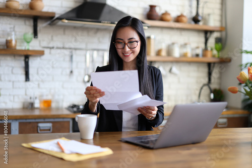 Obraz na płótnie An Asian businesswoman happily reads a finance letter at her desk, managing paperwork in her office