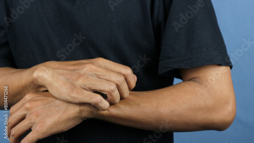 Asian young man scratching his hand isolated on blue background. photo