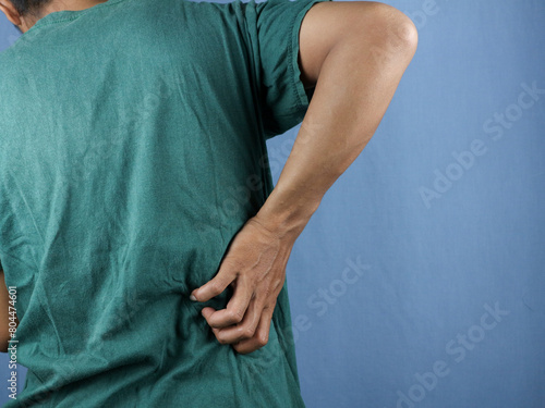 Asian young man scratching his back isolated blue background photo