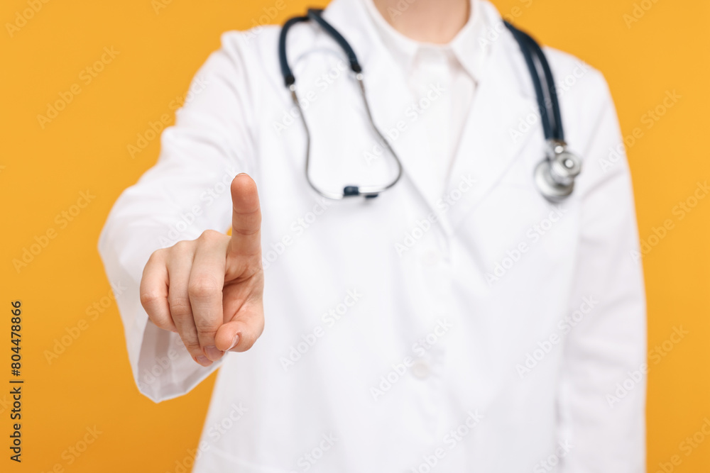 Doctor with stethoscope pointing on orange background, closeup Doctor with stethoscope pointing on orange background, closeup