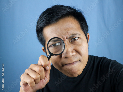 Funny Expression asian man looking through magnifying glass, searching or investigating something