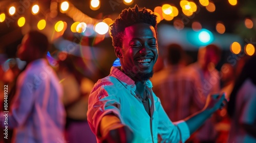 A young man is dancing at a party. He is smiling and has his eyes closed. He is wearing a white shirt and black pants. The background is blurry and out of focus.