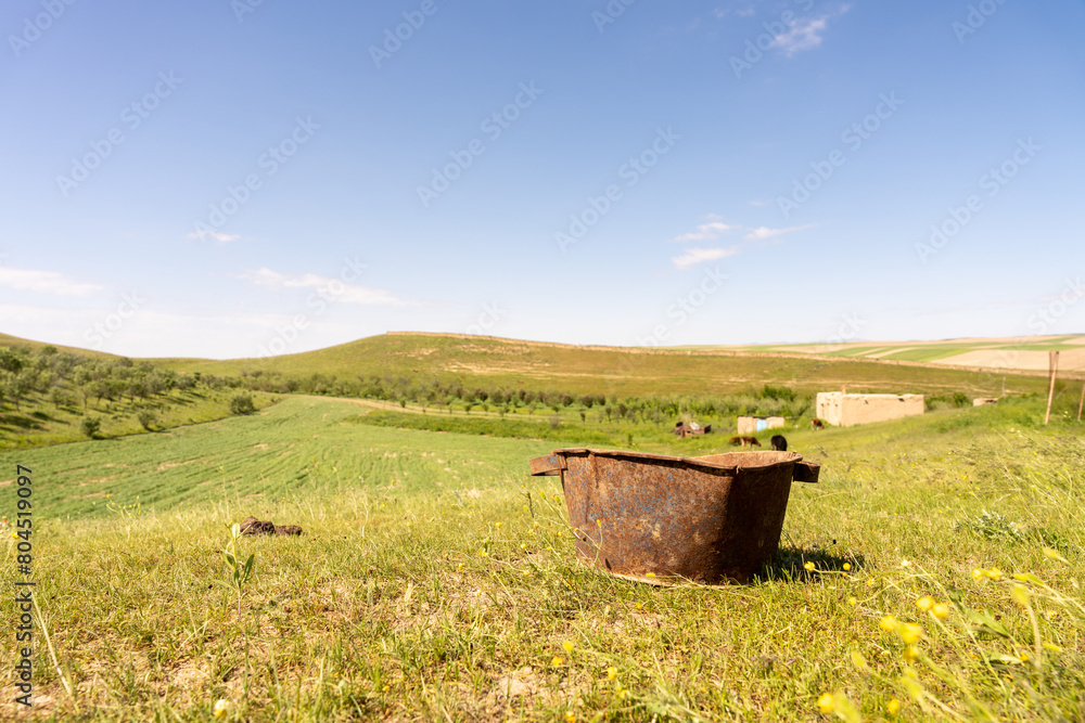 A rusty bucket is sitting on a grassy hillside. The sky is clear and the sun is shining brightly A rusty bucket is sitting on a grassy hillside. The sky is clear and the sun is shining brightly