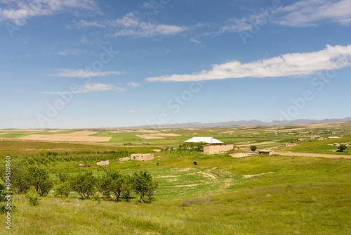 A large field with a small house in the middle. The sky is blue and there are no clouds