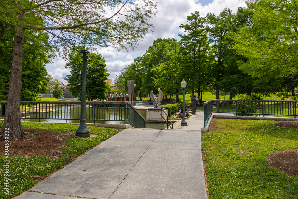a gorgeous spring landscape at Louis Armstrong Park with lush green trees, plants and grass, a lake, blue sky and clouds in New Orleans Louisiana USA