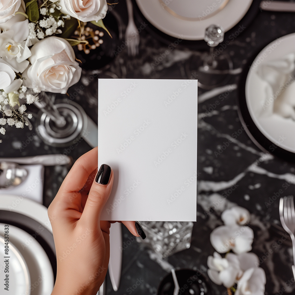 Obraz premium Blank paper card in hand over blurred elegant table setting background.