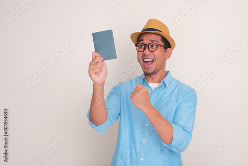 A man clenched fist showing excited expression while looking to passport that he hold photo