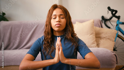 Latin woman with closed eyes enjoys yoga exercise at home