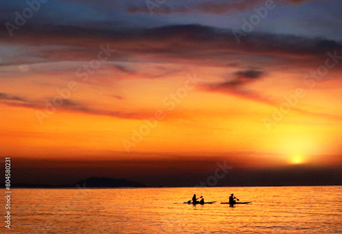 Silhouette of two people kayaking on the sea at sunset, young couple on a kayak on the sea at dusk under the light of the big moon Actively rest Swim away from problems privacy concept. - image