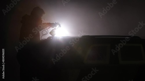 Automotive paint, Primer application, Texture effects. Person's shadowy figure is spotlighted while spray painting car, thanks to backlight that contrasts with misty scene. photo