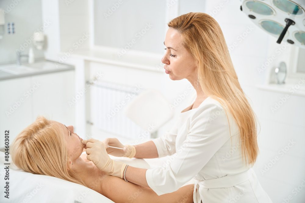 Fototapeta premium Qualified cosmetologist making microinjections into female chin