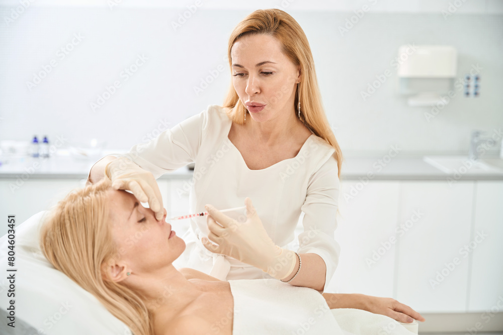 Cosmetologist making injections of filler to female client, contouring procedure Cosmetologist making injections of filler to female client, contouring procedure