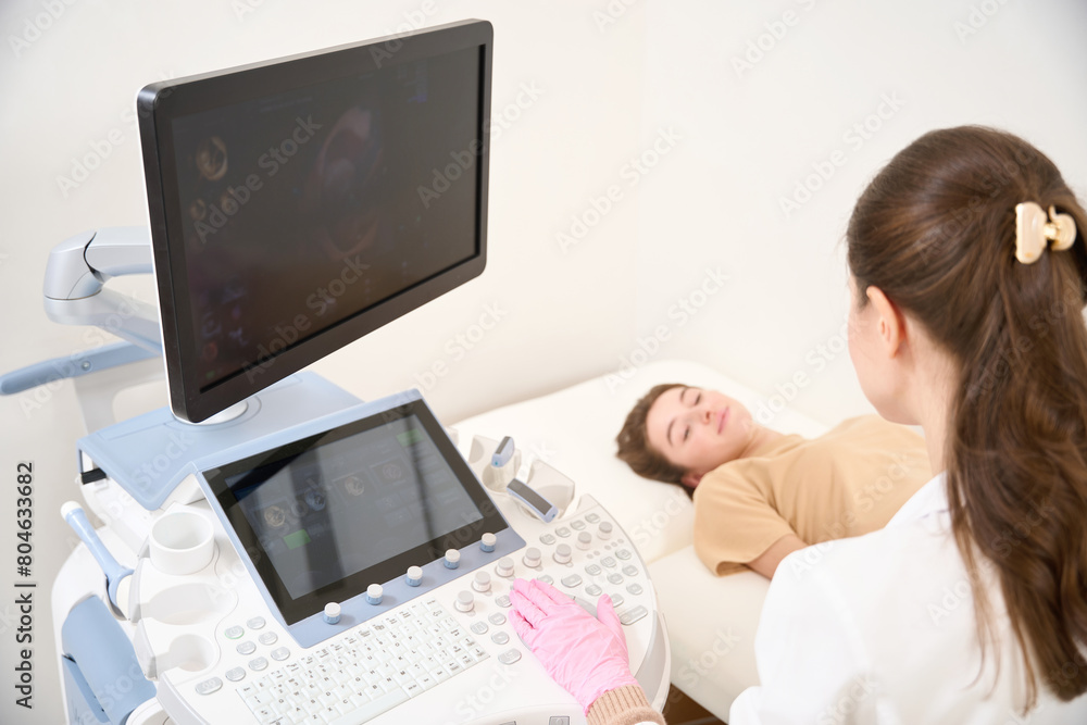 Female gynecologist doing ultrasound scanning of pregnant belly of blurred woman