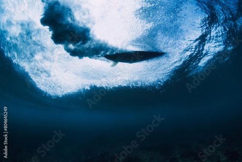 Surfer on surfboard in ocean underwater. Crashing wave and surfboard in transparent water