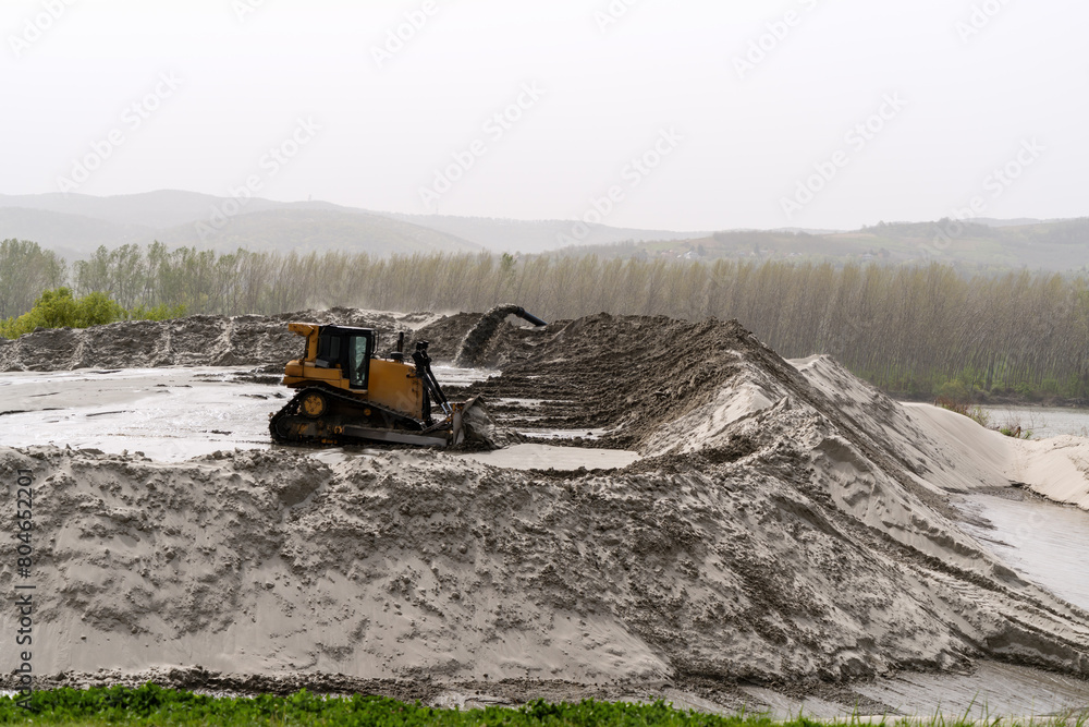 Sand mining industry. A mining bulldozer works on a huge pile of sand extracted from a river. Sand mining industry. A mining bulldozer works on a huge pile of sand extracted from a river.