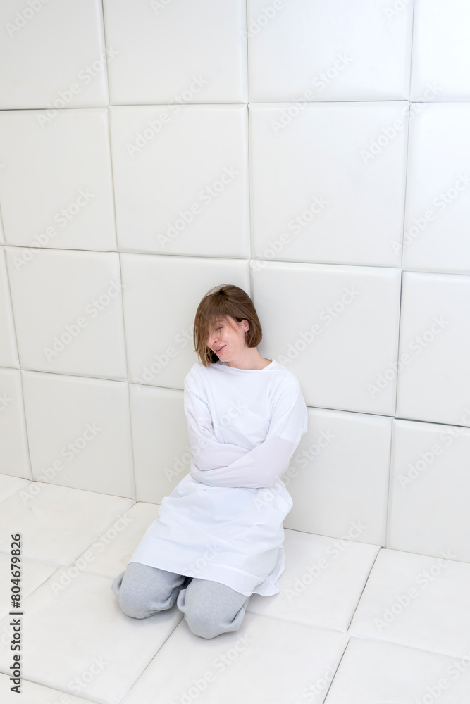 Young frustrated girl in a straitjacket is in an isolated white room in a mental hospital Young frustrated girl in a straitjacket is in an isolated white room in a mental hospital