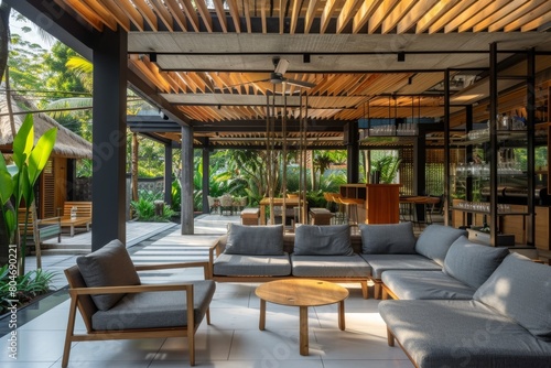 A modern Balinese hotel lounge with a wooden slat ceiling, dining area and bar in the background The room has grey fabric sofas and chairs on a white tile floor Generative AI